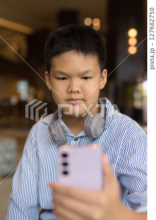 Thai boy using phone at cafe with headphones Thai boy using phone at cafe with headphones 127682750