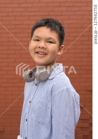 Thai boy in formal shirt with headphones posing against brick wall Thai boy in formal shirt with headphones posing against brick wall 127682758