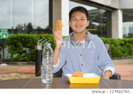 Thai boy eating fried chicken with headphones at outdoor table 127682762