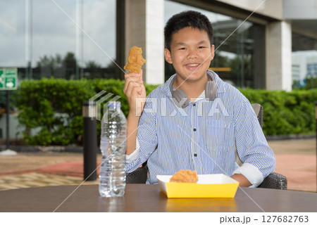 Thai boy eating fried chicken with headphones at outdoor table 127682763