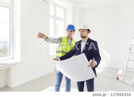 Two men in helmets with a drawing of the building inspect the premises 127682918