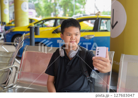 Thai teen boy wearing headphones using phone with city taxis in background Thai teen boy wearing headphones using phone with city taxis in background 127683047