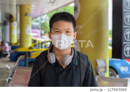 Thai boy with facial mask with taxis in background wearing headphones Thai boy with facial mask with taxis in background wearing headphones 127683060