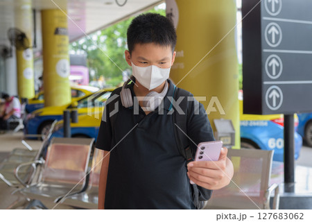 Thai boy with facial mask with taxis in background wearing headphones 127683062