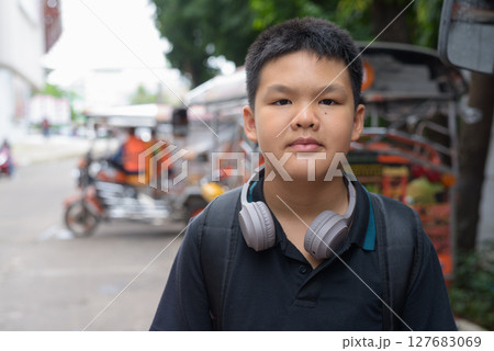 Thai boy with headphones standing by tuk tuk taxis Thai boy with headphones standing by tuk tuk taxis 127683069
