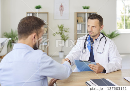 Friendly doctor shaking hands with a young patient sitting in medical clinic 127683151