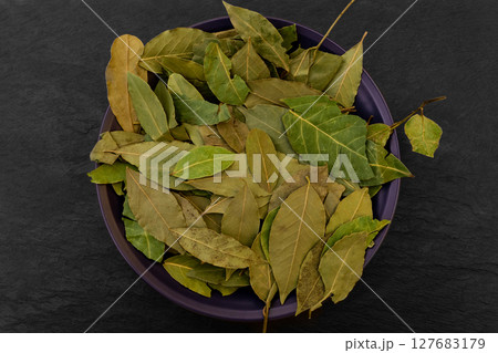 Dried up Bay Leaves Placed in Purple Plate on Black Stone Surface Background Dried up Bay Leaves Placed in Purple Plate on Black Stone Surface Background 127683179