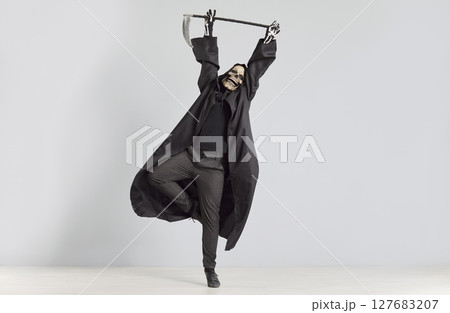 Man dressed as Grim Reaper, complete with black robe and skull mask, dances with scythe in hands. Man dressed as Grim Reaper, complete with black robe and skull mask, dances with scythe in hands. 127683207