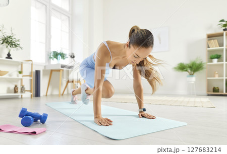Sporty athletic young woman doing mountain climber exercise in plank pose, having workout at home. Sporty athletic young woman doing mountain climber exercise in plank pose, having workout at home. 127683214