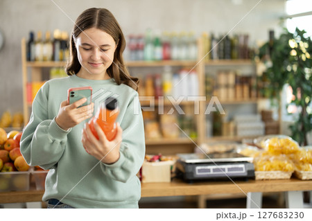 European teen girl customer at shop scans QR code on grapefruit juice bottle using phone camera European teen girl customer at shop scans QR code on grapefruit juice bottle using phone camera 127683230
