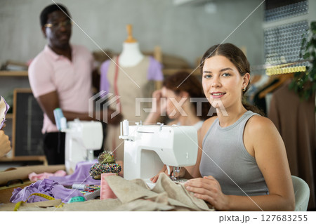 Positive girl working at machine during group sewing course for adults 127683255