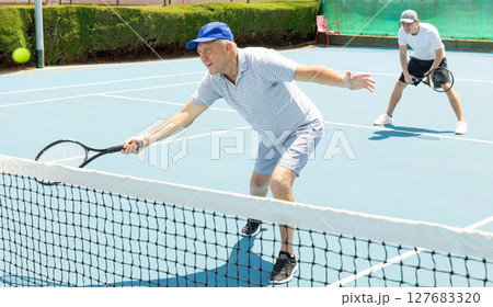 Elderly male player serving ball during training tennis in court outdoors 127683320