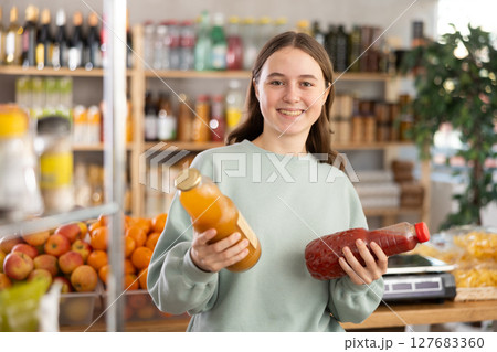 Teen girl hold packages bottles and choose consider juice in store 127683360