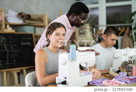 Middle-aged male teacher helping students sew 127683380