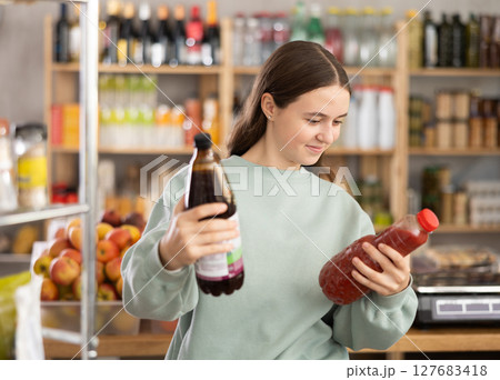 Teen girl hold packages bottles and choose consider juice in store 127683418