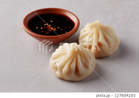 Chinese Dumplings with Pleated Tops and Dipping Sauce on Gray Background 127684283