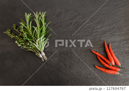 Thyme, Rosemary Bundles and Chili Peppers on Black Stone Surface Background 127684767