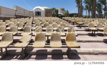 Rows of old, sun-bleached plastic seats in an outdoor arena on a sunny summer day. Waiting for an outdoor event or concert. Rows of old, sun-bleached plastic seats in an outdoor arena on a sunny summer day. Waiting for an outdoor event or concert. 127684988