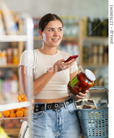 European woman customer at shop scans QR code on pickled tomatoes jar using phone camera European woman customer at shop scans QR code on pickled tomatoes jar using phone camera 127686041