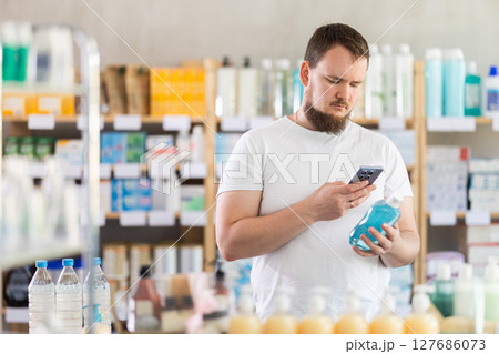 Man in summer clothes scans code on medicinal mouthwash to check expiration date Man in summer clothes scans code on medicinal mouthwash to check expiration date 127686073