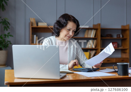 Middle aged senior woman sit with laptop and paper document. Pensive older mature lady reading paper bill pay online at home managing bank finances calculating taxes planning loan debt pension payment Middle aged senior woman sit with laptop and paper document. Pensive older mature lady reading paper bill pay online at home managing bank finances calculating taxes planning loan debt pension payment 127686100