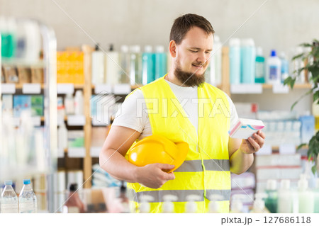Young man builder chooses pills at pharmacy 127686118