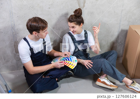 House decoration DIY renovation concept. Happy couple sitting on floor in empty room of new home planning design. Husband and wife holding swatch palette choosing colors for painting wall in new house House decoration DIY renovation concept. Happy couple sitting on floor in empty room of new home planning design. Husband and wife holding swatch palette choosing colors for painting wall in new house 127686124