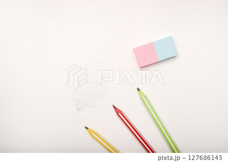 Three colored pencils and an eraser on white paper. Three colored pencils and an eraser on white paper. 127686143