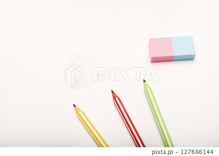Three colored pencils and an eraser on white paper. Three colored pencils and an eraser on white paper. 127686144