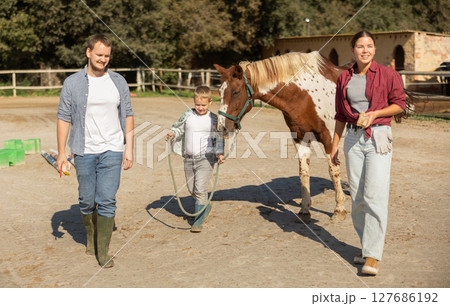 Father, mother and son riding horse together at small horse farm 127686192