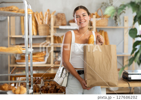 Positive young girl holding baguettes in paper bag in bakery Positive young girl holding baguettes in paper bag in bakery 127686202