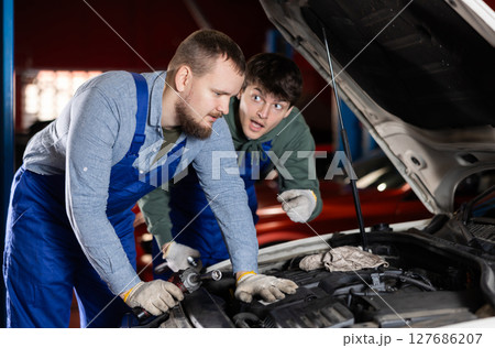 Two auto mechanics work together to diagnose an engine under the hood of a car in repair shop Two auto mechanics work together to diagnose an engine under the hood of a car in repair shop 127686207