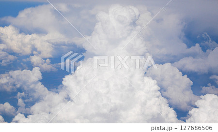 Large snow-white cumulus clouds against the background of a blue sky, view from the window of an airplane. 127686506