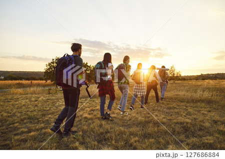 Group male and female Caucasian tourists walk in row one after other on flat green lawn. 127686884