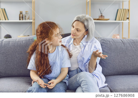 Senior grandmother sitting on sofa at home with her little granddaughter child girl and talking Senior grandmother sitting on sofa at home with her little granddaughter child girl and talking 127686908