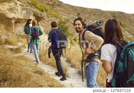 Portrait of smiling male hiker with backpack walking to top of mountain with his fellow hikers. Portrait of smiling male hiker with backpack walking to top of mountain with his fellow hikers. 127687128