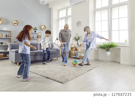 Active seniors loving elderly grandparents have fun playing ball with little children in living room Active seniors loving elderly grandparents have fun playing ball with little children in living room 127687235