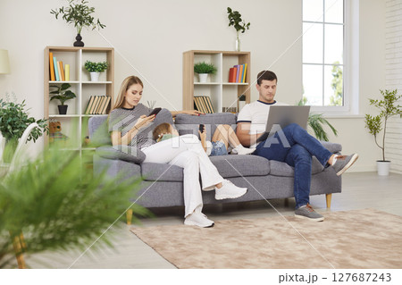Family Using Laptops And Phones During Leisure Time On The Sofa At Home 127687243