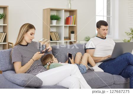Young family relaxing on sofa, using laptop and smartphones, spending quality time together at home. 127687275