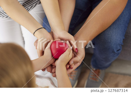 Top view of young family holding red heart in hands together sitting at home. Top view of young family holding red heart in hands together sitting at home. 127687314