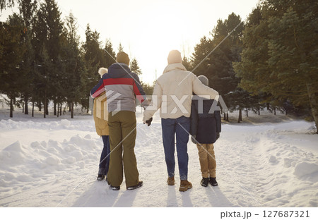 Back view of family of four enjoying nature in winter park walking outdoors. 127687321