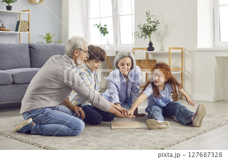 Senior grandparents and grandchildren putting hands in a stack finishing collecting puzzle at home Senior grandparents and grandchildren putting hands in a stack finishing collecting puzzle at home 127687328