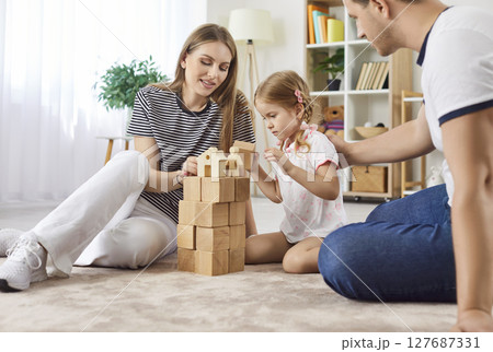 Parents playing an educational game with child girl in the living room at home together. 127687331