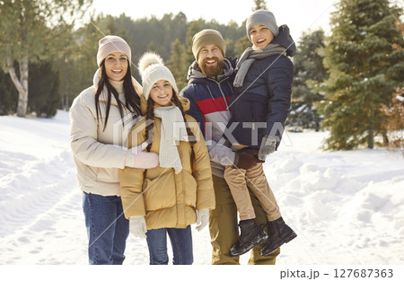 Portrait of happy family with two children posing together during walk in winter snowy park. 127687363