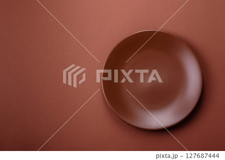 Empty ceramic plate on a monochrome brown background Empty ceramic plate on a monochrome brown background 127687444
