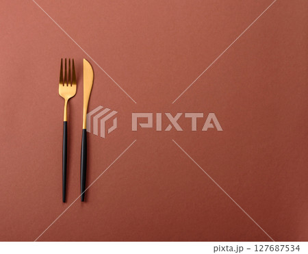 Knife and fork, cutlery on a brown dining table Knife and fork, cutlery on a brown dining table 127687534