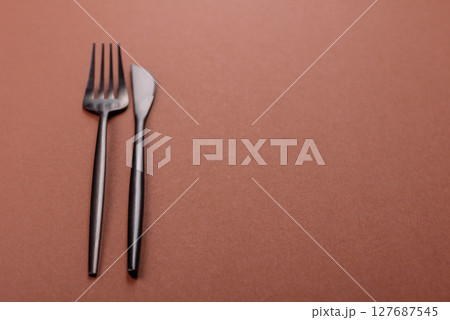 Knife and fork, cutlery on a brown dining table Knife and fork, cutlery on a brown dining table 127687545