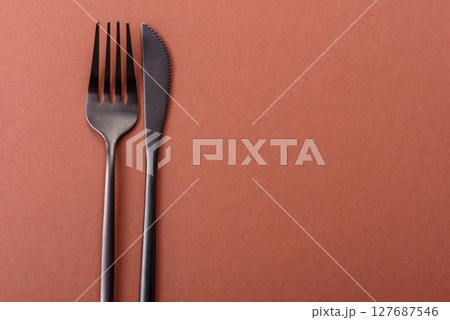 Knife and fork, cutlery on a brown dining table Knife and fork, cutlery on a brown dining table 127687546