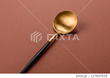 Empty metal spoon on a monochrome brown background 127687639