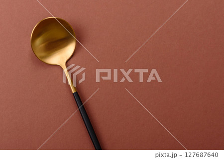 Empty metal spoon on a monochrome brown background 127687640